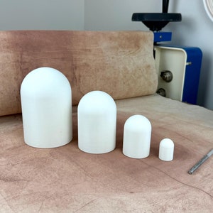May include: Four white ceramic dome-shaped objects of varying sizes, arranged from largest to smallest on a brown surface.