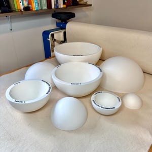 May include: A collection of white ceramic bowl molds in various sizes, each featuring the text Moonmoon Ceramics and specific measurements in inches, such as 4 inches, 6 inches, 8 inches, and 10 inches, arranged on a light-colored fabric surface.