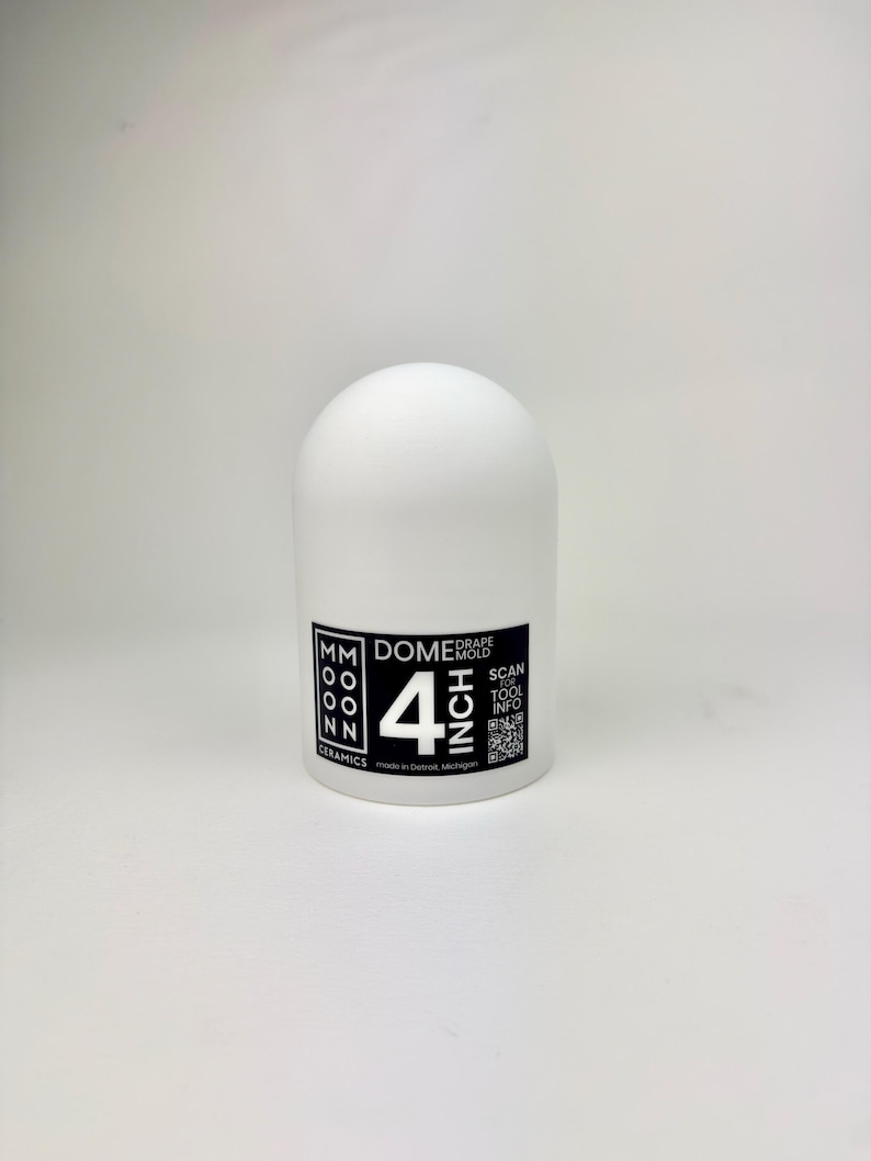 Op de afbeelding: Een witte keramische dome-mal met een diameter van ongeveer 10 cm. Het product heeft een afgeronde bovenkant en een cilindrische basis. Het label luidt "MM Moon Ceramics" en "Drape Mold". Inclusief een QR-code en de tekst "Scan Tool Info". Gemaakt in Detroit, Michigan.