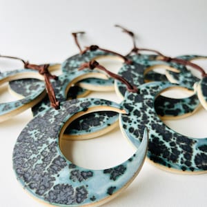 May include: A group of ceramic crescent moon ornaments with a blue and black speckled glaze. The ornaments have brown leather cords attached to them.