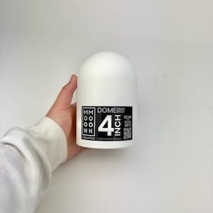 Op de afbeelding: Een wit keramisch koepelvormig object met een zwart-wit label met de tekst "4 INCH". Het label bevat ook de tekst "MM MOON NN CERAMICS" en "DOME MOLD". Het object wordt door een persoon vastgehouden.