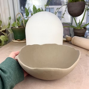 May include: A large, light brown ceramic bowl with a wavy rim. The bowl is sitting on a light brown surface.