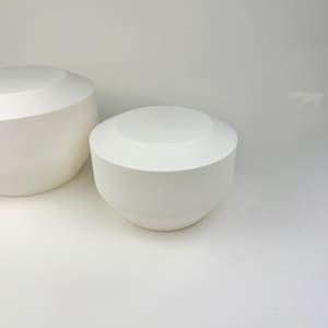May include: Two matte white bowls with a smooth, rounded silhouette and a flat top edge. The bowls feature a wide, circular opening that tapers down toward a narrow base, presenting a clean, uniform appearance without any decorative patterns.