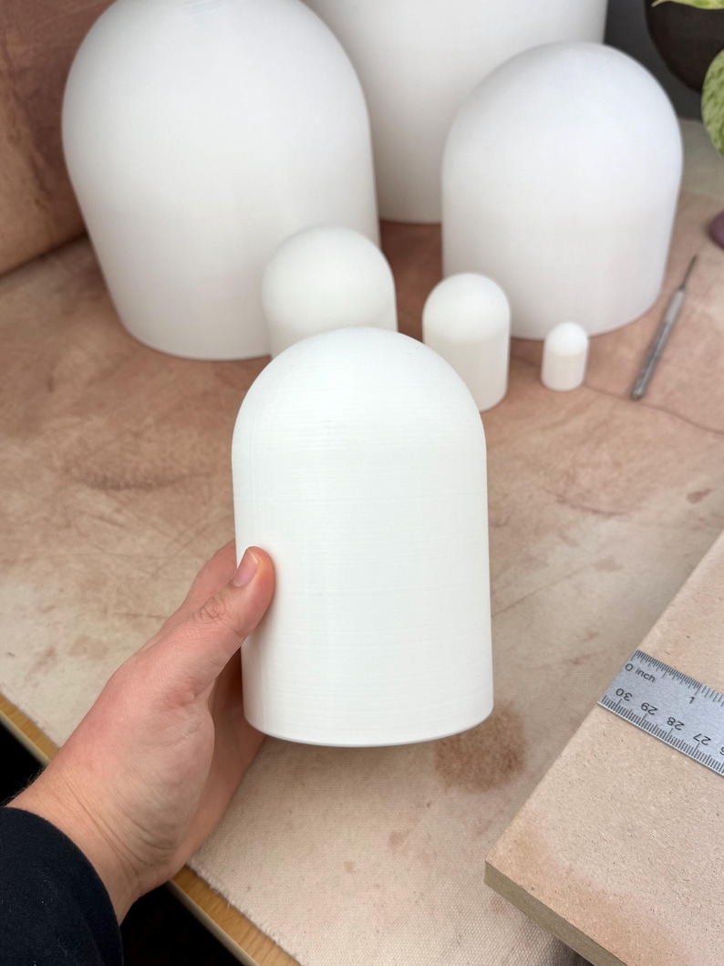 May include: A set of five white ceramic dome-shaped objects of varying sizes. The largest dome is in the background and the smallest dome is in the foreground. The domes are arranged in a staggered pattern. A ruler is visible in the bottom right corner of the image.