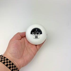 May include: A white, circular ceramic tool labeled Moonmoon Ceramics 3" Shroom Puck, Double-Sided Drape Form, with a QR code and text indicating it was made in Detroit, Michigan. The object is smooth, round, and features black printed text.