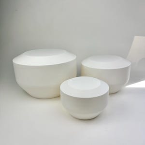 May include: A set of three ceramic mugs with a speckled, matte finish in cream, light grey, and dark grey. Each mug has a simple, minimalist design, suitable for coffee or tea.