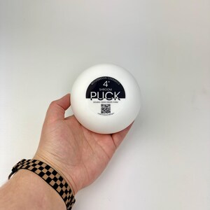 May include: A white, circular ceramic drape form with a black label in the center. The label reads MOONMOON CERAMICS 4" SHROOM PUCK DOUBLE-SIDED DRAPE FORM and includes a QR code. The object is a smooth, solid, rounded tool for pottery shaping.