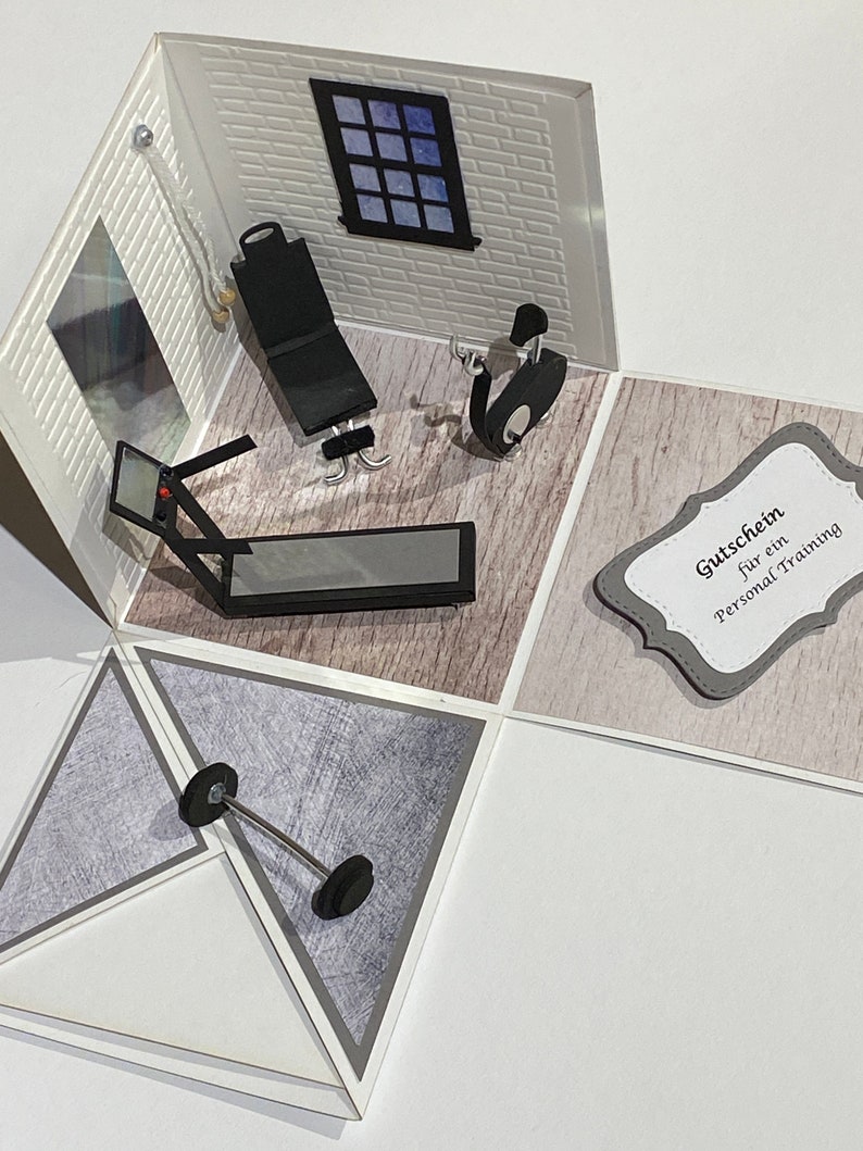 May include: A handmade pop-up card depicting a miniature gym. The card includes a treadmill, weight bench, stationary bike, and a barbell. The walls are white brick, and a window shows a blue sky. A gift certificate is also included.