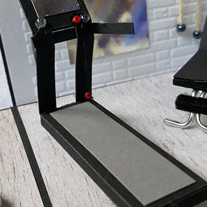 May include: A miniature black treadmill with a grey running surface and a silver display. The treadmill has red and clear accents, set against a white brick wall. A small black exercise bench is visible.