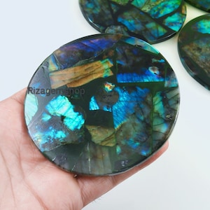 May include: Six round coasters made of iridescent labradorite stone. The coasters are a mix of blue, green, and gold colours. The coasters are arranged in a circle with one coaster in the centre.