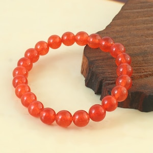 May include: A red gemstone bracelet with round beads. The bracelet is on a wooden surface.