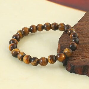 May include: A brown and gold tiger's eye beaded bracelet. The bracelet is made of round beads and is strung on a clear elastic cord.