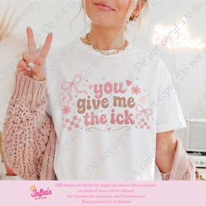 Puede incluir: Camiseta blanca con la frase "you give me the ick" en letras rosas y marrones. El diseño incluye lazos, flores, corazones y un patrón de cuadros. La camiseta forma parte de una colección de diseño digital.