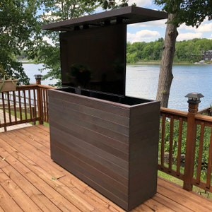 May include: A dark brown wooden cabinet with a built-in television that is mounted on a retractable arm. The cabinet is on a wooden deck overlooking a lake.