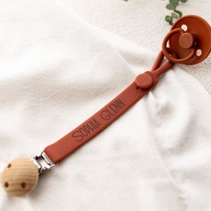 May include: A terracotta silicone pacifier clip with a wooden bead and a personalized name tag that reads "Sophia Glenn".