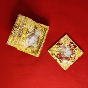 May include: Two decorative square resin pieces with gold leaf accents and a white fluffy center, set against a red background. One piece is a tray, the other a coaster.
