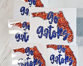 May include: Five stickers with a glittery orange outline of the state of Florida and the text "Go Gators" in blue glitter.