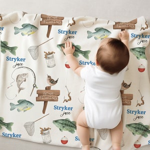 Puede incluir: Una manta de beb&eacute; blanca con tem&aacute;tica de pesca. La manta presenta un patr&oacute;n repetitivo de peces, ca&ntilde;as de pescar, gusanos y un letrero que dice "Gone Fishing". La manta est&aacute; personalizada con el nombre "Stryker Jace".