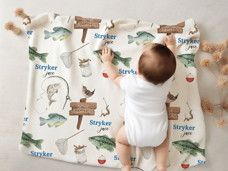 Puede incluir: Una manta de beb&eacute; blanca con tem&aacute;tica de pesca. La manta presenta un patr&oacute;n repetitivo de peces, ca&ntilde;as de pescar, gusanos y un letrero que dice "Gone Fishing". La manta est&aacute; personalizada con el nombre "Stryker Jace".