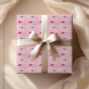May include: Pink gift wrap with a white bow. The wrapping paper has a repeating pattern of colorful balloons and the text "Happy Birthday Linsey".