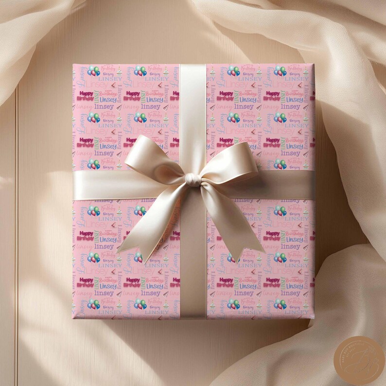 May include: Pink gift wrap with a white bow. The wrapping paper has a repeating pattern of colorful balloons and the text "Happy Birthday Linsey".