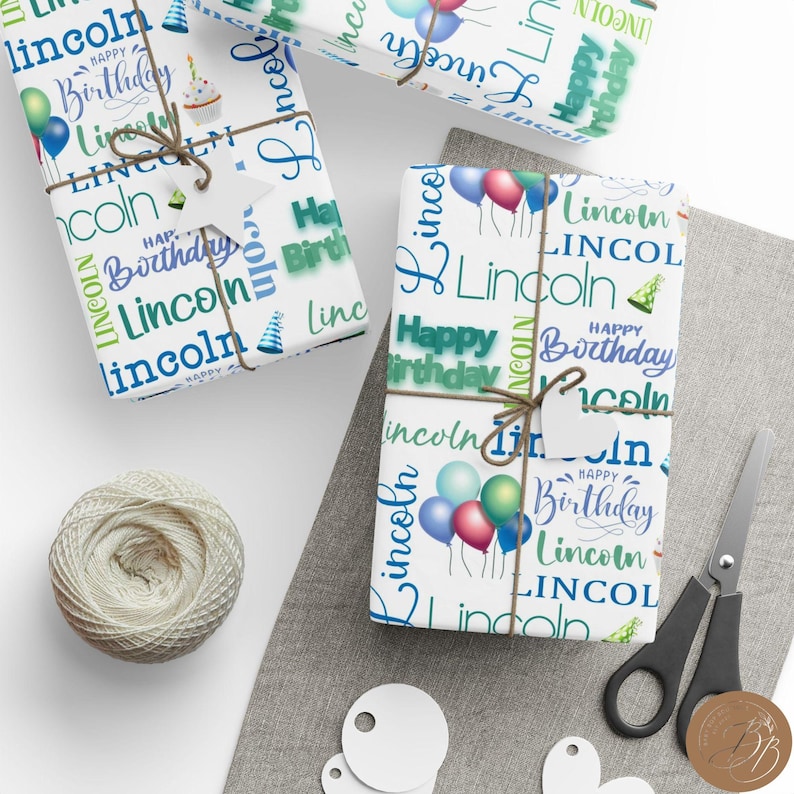 May include: White wrapping paper with a blue and green pattern featuring the name "Lincoln" and the phrase "Happy Birthday" repeated throughout. The paper is wrapped around a gift box with a brown twine bow.