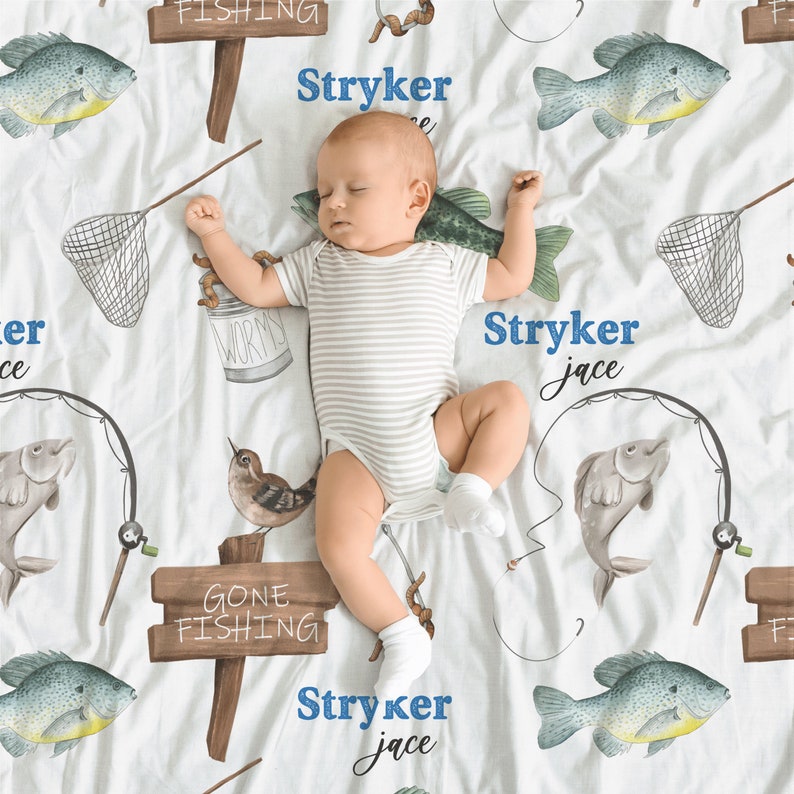 Puede incluir: Una manta de beb&eacute; blanca con tem&aacute;tica de pesca. La manta presenta una variedad de im&aacute;genes relacionadas con la pesca, incluyendo peces, ca&ntilde;as de pescar, gusanos y una red. La manta tambi&eacute;n tiene el nombre "Stryker Jace" escrito tres veces.