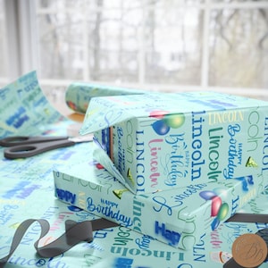 May include: A stack of two gift boxes wrapped in blue and white wrapping paper with the name "Lincoln" and the words "Happy Birthday" repeated on the paper.