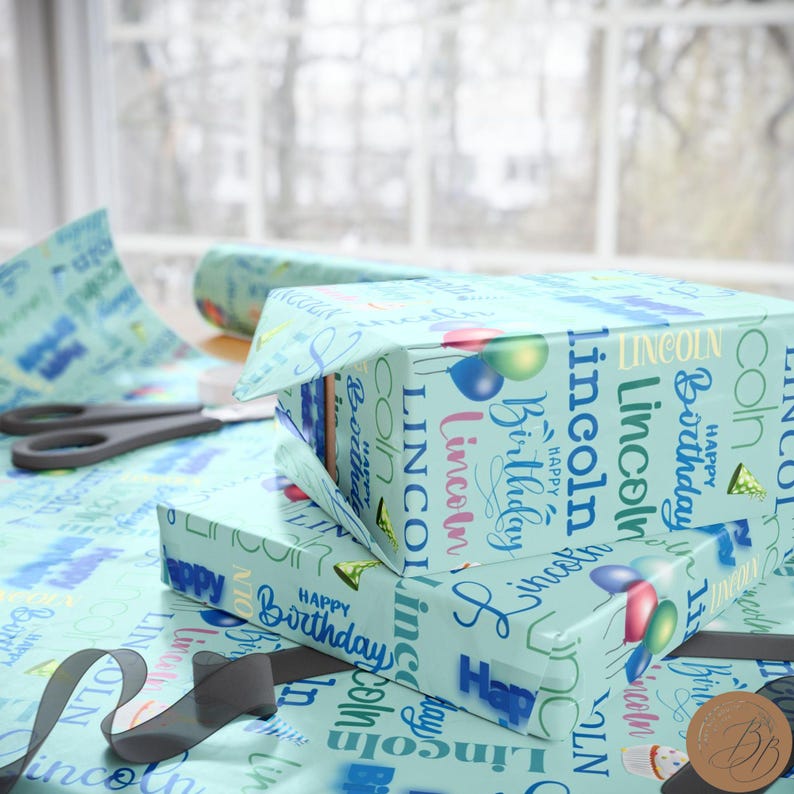 May include: A stack of two gift boxes wrapped in blue and white wrapping paper with the name "Lincoln" and the words "Happy Birthday" repeated on the paper.