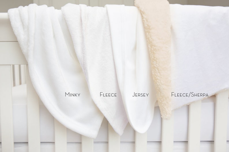Puede incluir: Cuatro mantas blancas para beb&eacute; expuestas en una barandilla de cuna blanca. Las mantas est&aacute;n etiquetadas como "Minky", "Fleece", "Jersey" y "Fleece/Sherpa".