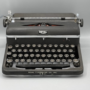 May include: A black Royal typewriter with a silver carriage return lever and a black and gold keyboard. The typewriter has the words "Royal Typewriter Co. Inc. U.S.A." printed on the front.