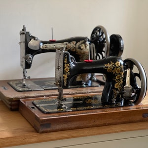 May include: Two vintage black sewing machines with floral designs on the side, sitting on wooden bases.