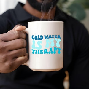 May include: White ceramic mug with a blue and white graphic that says "Cold Water Is My Therapy".