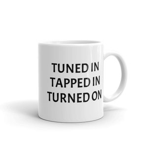 May include: White ceramic coffee mug with black text that reads "Tuned In Tapped In Turned On".