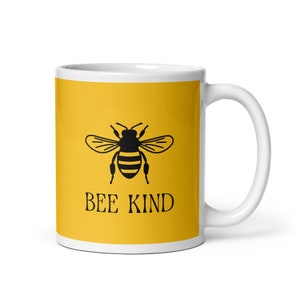 May include: White ceramic mug with a yellow background featuring a black bee illustration and the words "BEE KIND" in black. The mug has a white handle and a glossy finish.