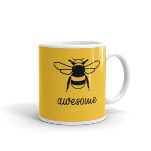 May include: White ceramic mug with a yellow background featuring a black illustration of a bee and the word "awesome" in a handwritten font. The mug has a white handle and a white interior.