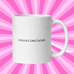 May include: White ceramic mug with the word "overstimulated" printed in black text on the front.
