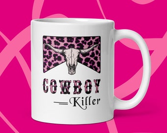 May include: White ceramic mug with a pink and black leopard print design featuring a cow skull. The text "COWBOY - Killer" is printed below the design.