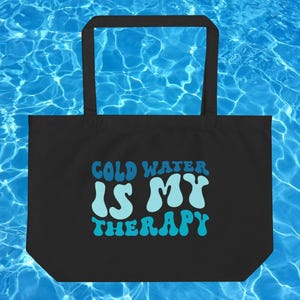Może przedstawiać: Czarna torba typu tote z napisem "COLD WATER IS MY THERAPY" w kolorze niebieskim i jasnoniebieskim. Torba ma prostokątny kształt z dużym otworem i dwoma uchwytami. Tło to niebieski wz&oacute;r wody.