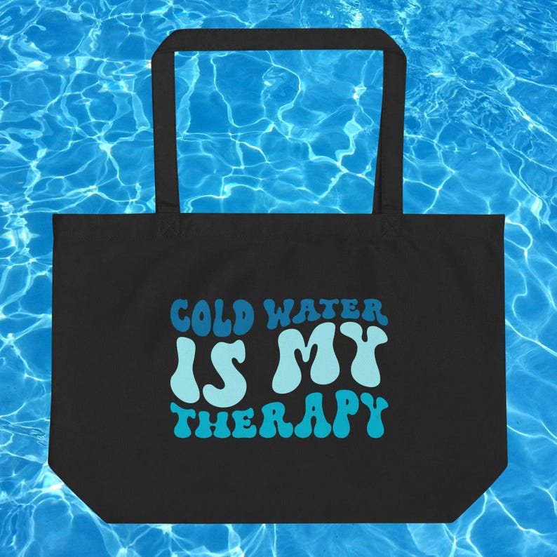 Może przedstawiać: Czarna torba typu tote z napisem "COLD WATER IS MY THERAPY" w kolorze niebieskim i jasnoniebieskim. Torba ma prostokątny kształt z dużym otworem i dwoma uchwytami. Tło to niebieski wz&oacute;r wody.