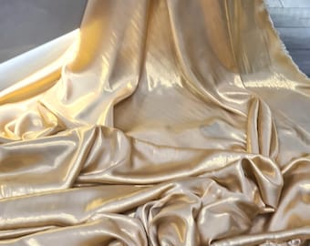 May include: A close-up shot of a luxurious, flowing fabric in a warm, golden color. The material has a silky, satin-like sheen, with soft folds and gentle shadows that create a sense of depth and movement. The fabric appears to be draped, suggesting it could be used for apparel or home decor.