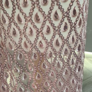 May include: Pink sequined fabric with a teardrop pattern. The sequins are arranged in a repeating pattern of teardrops, creating a shimmering effect.