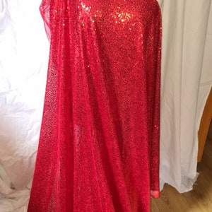 Peut inclure: Tissu de sequins rouge avec une finition chatoyante. Le tissu est drapé sur un mannequin.