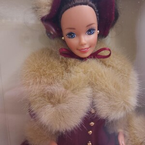 Peut inclure: Une poupée Barbie vintage portant une robe bordeaux avec un col en fausse fourrure et un chapeau assorti. La poupée a les cheveux bruns, les yeux bleus et un nœud rouge.