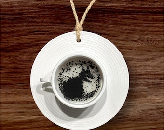 May include: A white ceramic teacup and saucer with a black silhouette of a fox in the bottom of the cup. The cup and saucer are hanging from a brown twine string.