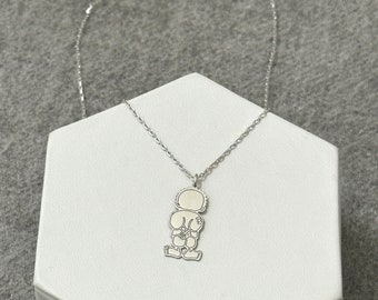 May include: A silver necklace with a pendant shaped like a child standing with their hands behind their back.