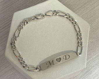 May include: Silver chain bracelet with a rectangular tag engraved with the initials "M" and "D" separated by a heart symbol.