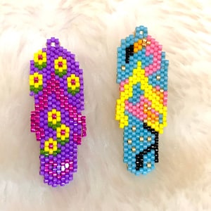 May include: Two beaded flip-flop charms, one purple with yellow flowers and one blue with pink and yellow accents.