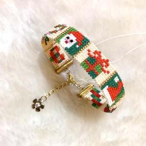 May include: A white beaded bracelet with a Christmas-themed design featuring red, green, and gold beads. The bracelet has a gold chain with a small flower charm.