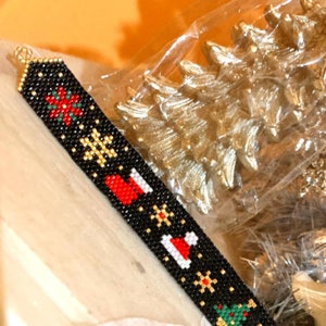 May include: A black beaded bracelet with a Christmas theme. The bracelet features red and white Santa hats, green Christmas trees, and gold snowflakes.